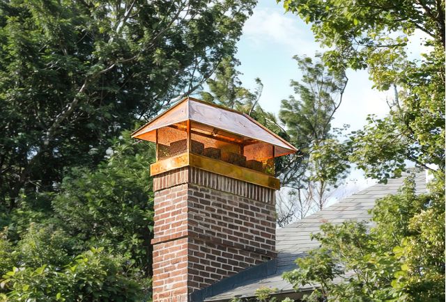 Residential brick chimney with chimney cap on shingle roof at dusk